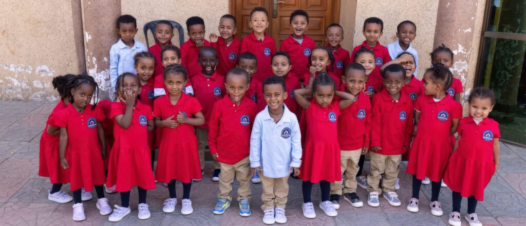 Large group of Ethiopian children in matching red and white school uniforms with Adera logos, standing together for education sponsorship program photo.