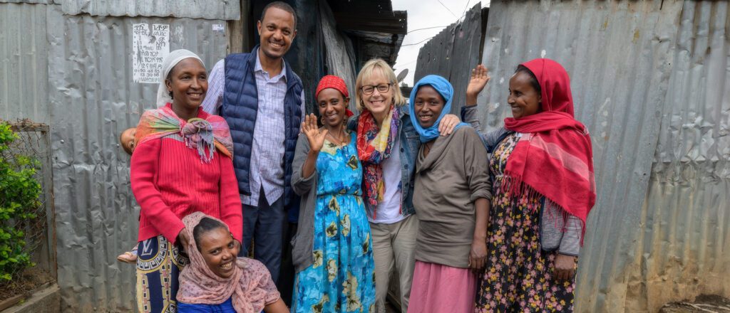 A group photo of Adera Foundation leadership standing together outdoors in front of corrugated metal walls typical of an Ethiopian community setting.