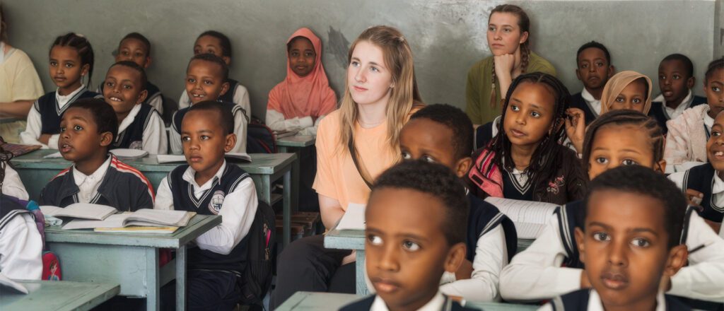 Classroom full of Ethiopian students in navy and white uniforms with two blonde volunteers sitting among them during short-term mission trip.